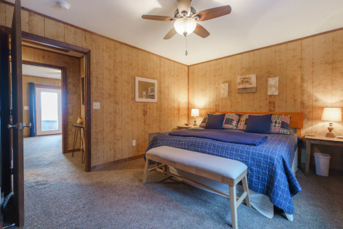 Cozy bedroom with a large bed, decorative pillows, a ceiling fan, and warm lighting, featuring a carpeted floor.