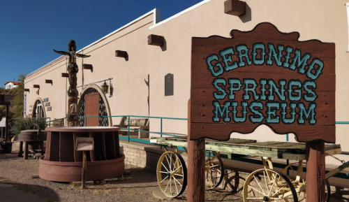 Sign for Geronimo Springs Museum in front of a southwestern-style building with vintage wagons and a totem pole.