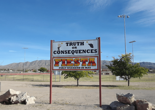 Sign for "Truth or Consequences Fiesta" with details about the event in May, set against a clear blue sky and mountains.
