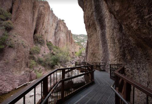 A metal walkway winds through a rocky canyon, surrounded by steep cliffs and sparse greenery.