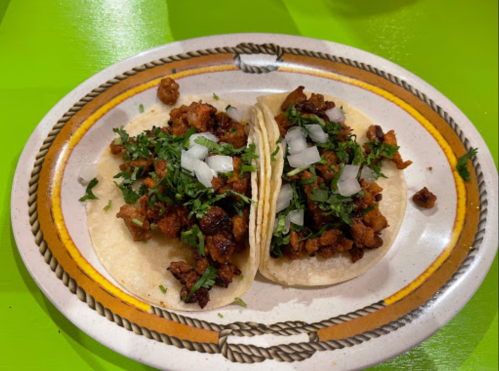 Two tacos filled with seasoned meat, topped with chopped onions and cilantro, served on a decorative plate.