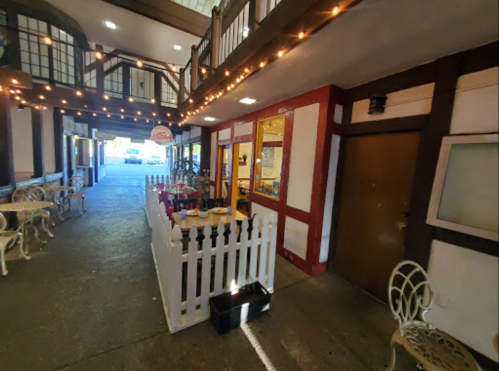 A charming walkway with string lights, featuring a white picket fence and decorative seating areas.
