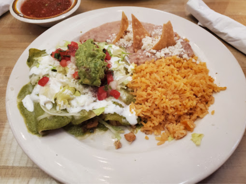 A plate of enchiladas topped with guacamole and sour cream, served with rice, refried beans, and tortilla chips.