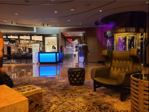 A modern hotel lobby with stylish seating, a reception desk, and a hallway leading to other areas. Soft lighting enhances ambiance.