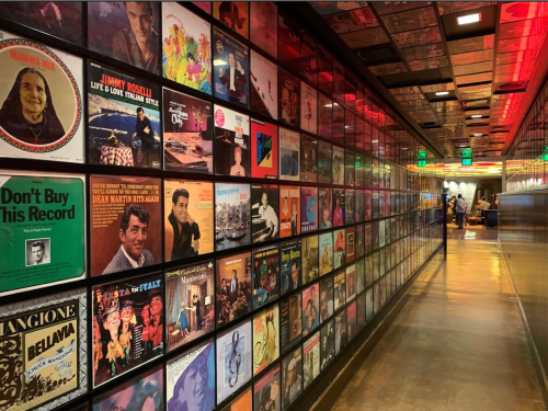 A hallway lined with colorful vinyl record covers, illuminated by vibrant lights, creating a nostalgic atmosphere.