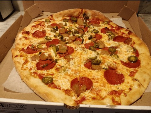 A large pizza in a box topped with pepperoni, sausage, and green olives.