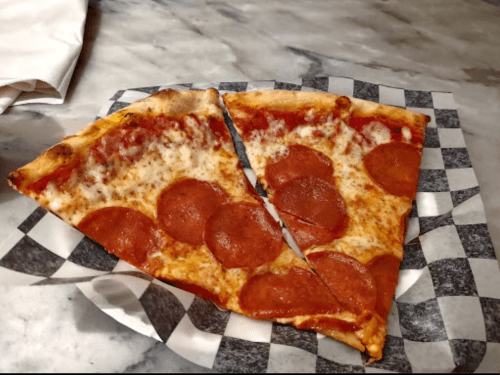 Two slices of pepperoni pizza on a black and white checkered paper, resting on a marble surface.