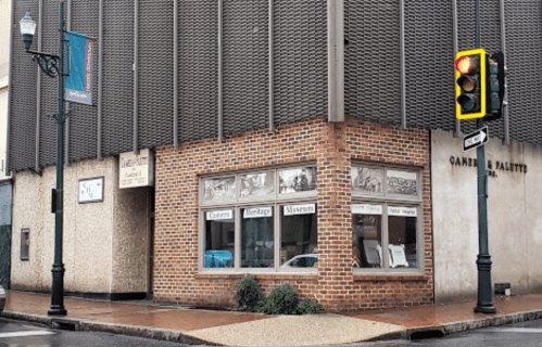 A brick building with large windows displaying museum exhibits, located at a street corner with a traffic light.