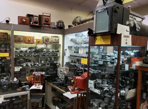 A collection of vintage cameras displayed in a museum, showcasing various models and styles in glass cases.
