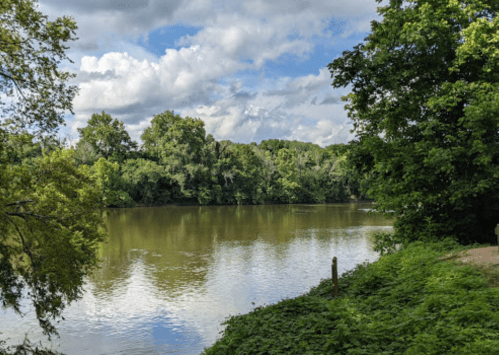 A serene river scene surrounded by lush greenery and trees under a partly cloudy sky.