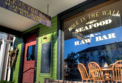 A colorful seafood market and raw bar with a green exterior and large windows displaying its name.