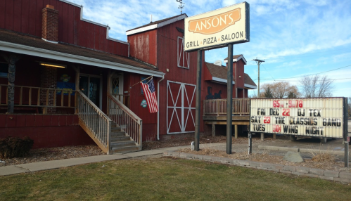 Exterior of Anson's Grill-Pizza Saloon with a sign and marquee displaying events, American flag, and rustic red building.