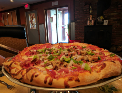 A large pizza topped with green peppers, onions, and meat, served on a silver platter in a cozy restaurant setting.