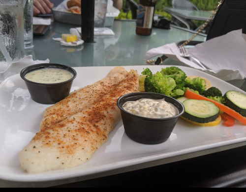 A plate with a fillet of fish, two sauces, and a side of steamed broccoli and mixed vegetables.