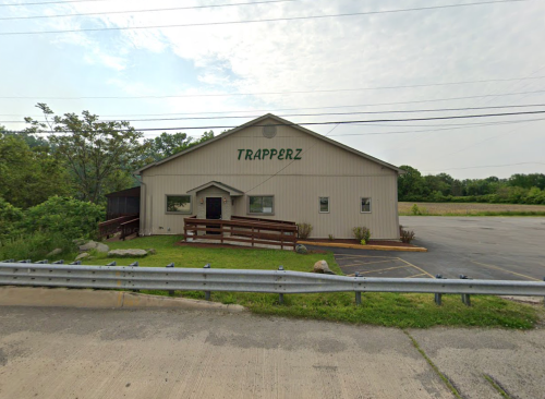 A large, light-colored building with "TRAPPERZ" written on it, surrounded by greenery and an empty parking lot.