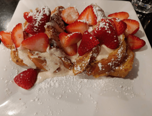 A plate of French toast topped with fresh strawberries and powdered sugar, drizzled with cream.