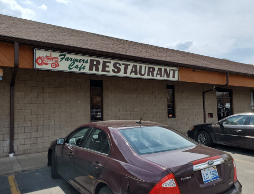 Exterior of Farmers Cafe Restaurant with a sign and parked cars in front.