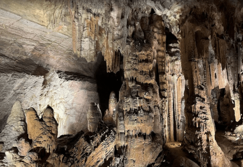 A dimly lit cave interior featuring large, intricate rock formations and stalactites hanging from the ceiling.