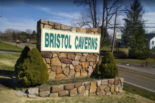 Sign for Bristol Caverns made of stone, surrounded by greenery, with a clear blue sky in the background.