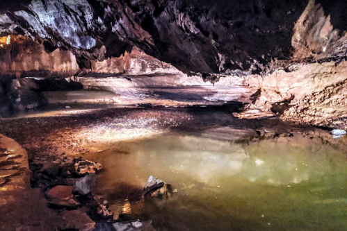 A dimly lit cave interior with a still, reflective pool of water and rocky walls.