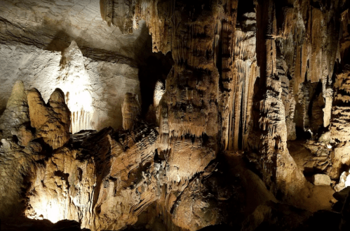 A dimly lit cave interior featuring impressive stalactites and stalagmites, showcasing natural rock formations.