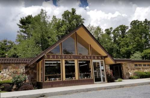 Exterior of Bristol Caverns visitor center, featuring large windows and stone walls, surrounded by trees and a cloudy sky.