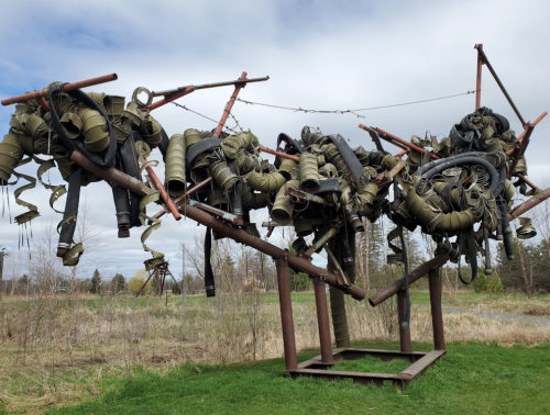 A large outdoor sculpture made of twisted metal and various hoses, resembling an abstract, tangled form against a cloudy sky.