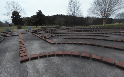 A winding path made of bricks in a park, surrounded by trees and open space.