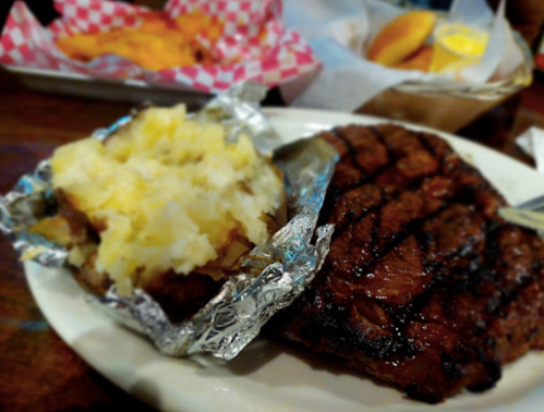 A plate featuring a grilled steak, a baked potato wrapped in foil, and a side of fries in a basket.