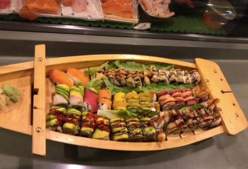 A wooden boat filled with various sushi rolls and sashimi, garnished with wasabi and sauces.
