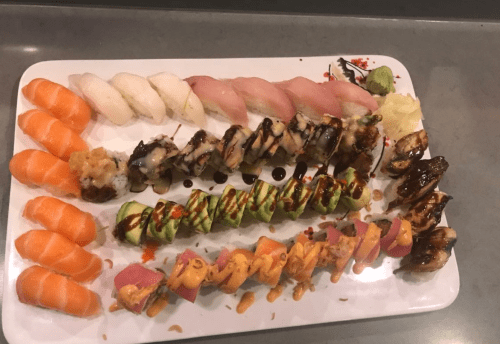 A platter of assorted sushi, including nigiri, rolls, and sashimi, arranged in colorful rows on a white plate.