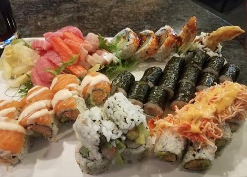 A colorful sushi platter featuring various rolls, sashimi, and garnishes on a white plate.
