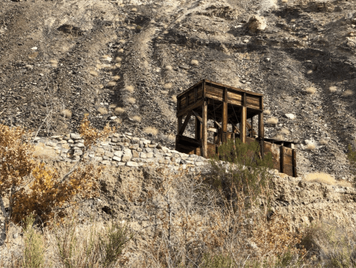 A wooden structure on a rocky hillside, surrounded by sparse vegetation and dry terrain.