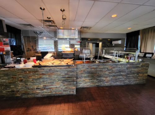 Interior of a restaurant featuring a buffet counter with various food options and a stone wall design.