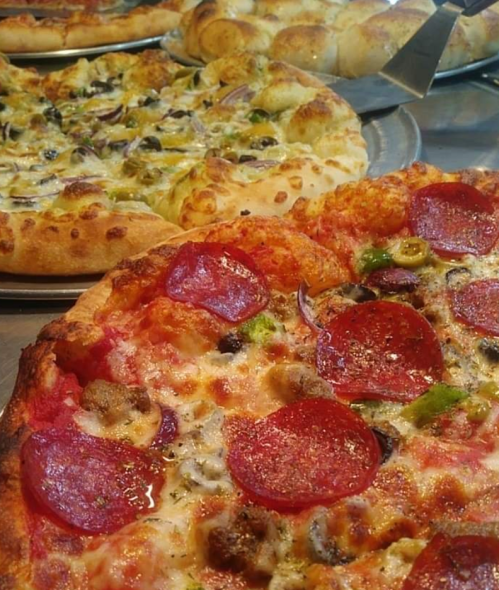 A close-up of a pepperoni pizza with green peppers and olives, with other pizzas in the background.