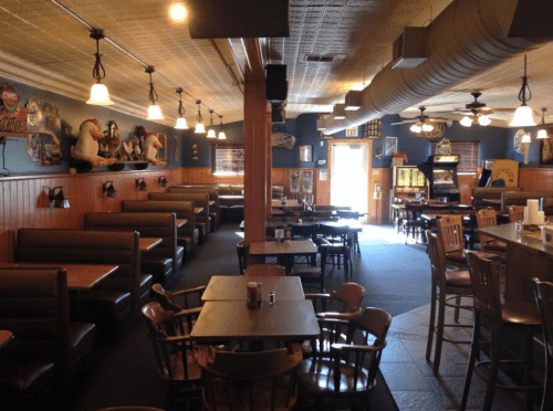 Cozy restaurant interior with wooden tables, chairs, and booths, featuring warm lighting and vintage decor.