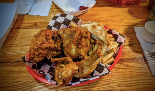 A red plate with fried chicken, crinkle-cut fries, and a piece of bread, all served on a checkered paper liner.