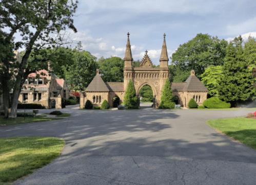 A grand stone entrance with towers, surrounded by greenery and a paved road leading into a serene landscape.
