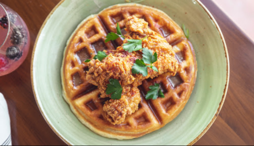 A plate of waffles topped with crispy fried chicken and garnished with fresh parsley.