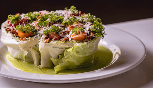 A vibrant salad served in a lettuce cup, topped with tomatoes, herbs, and cheese, on a green sauce base.