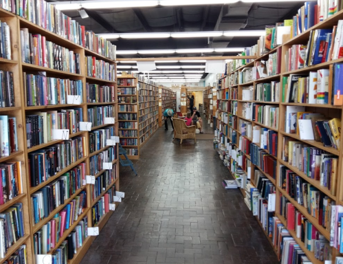 A cozy bookstore aisle lined with wooden shelves filled with books, leading to a seating area in the background.
