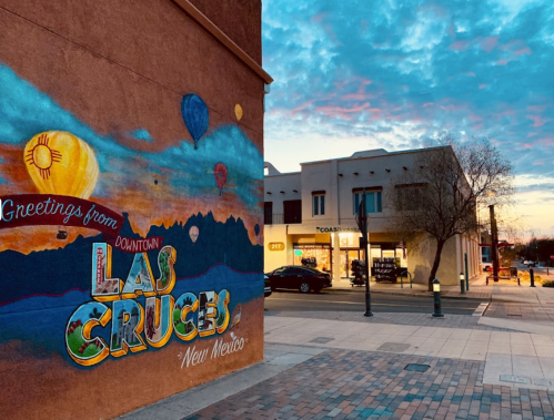 Colorful mural reading "Greetings from Downtown Las Cruces" with a sunset sky and buildings in the background.