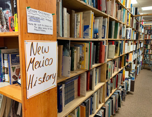 Bookshelves filled with various books, featuring a sign that reads "New Mexico History" on a wooden shelf.