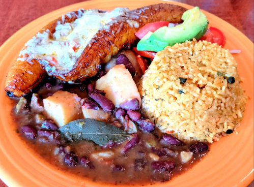 A colorful plate featuring rice, beans, fried plantains, avocado, and diced vegetables.
