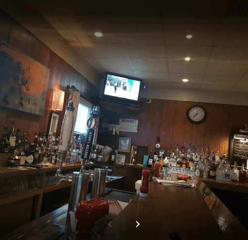 A cozy bar interior with a variety of liquor bottles, a TV showing a scene, and a clock on the wall.
