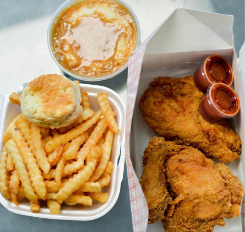 A takeout meal featuring crispy fried chicken, crinkle-cut fries, a biscuit, and a bowl of gravy.