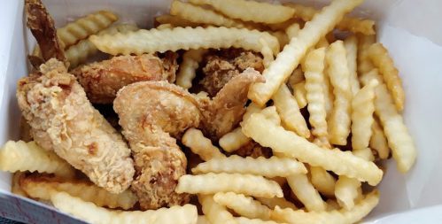 A takeout box filled with crispy fried chicken wings and crinkle-cut French fries.