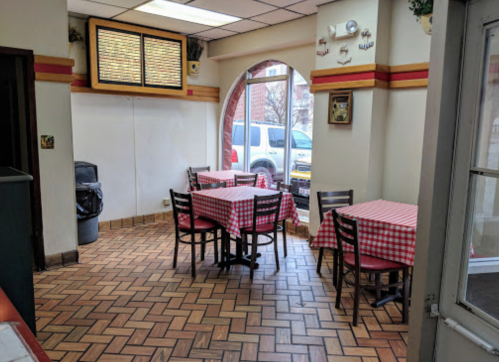 A small, empty restaurant interior with checkered tablecloths and a window view of parked cars outside.