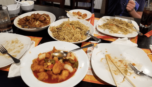 A table with several empty plates and bowls, featuring various Asian dishes like noodles, chicken, and shrimp.