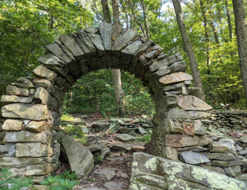 Stone archway surrounded by lush green trees and rocky terrain in a forested area.